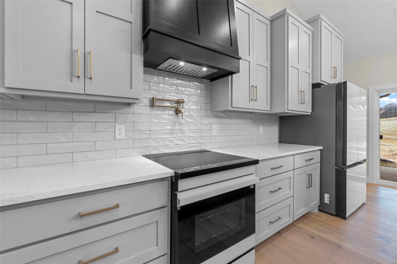 Kitchen featuring light stone counters, backsplash, premium range hood, and appliances with stainless steel finishes