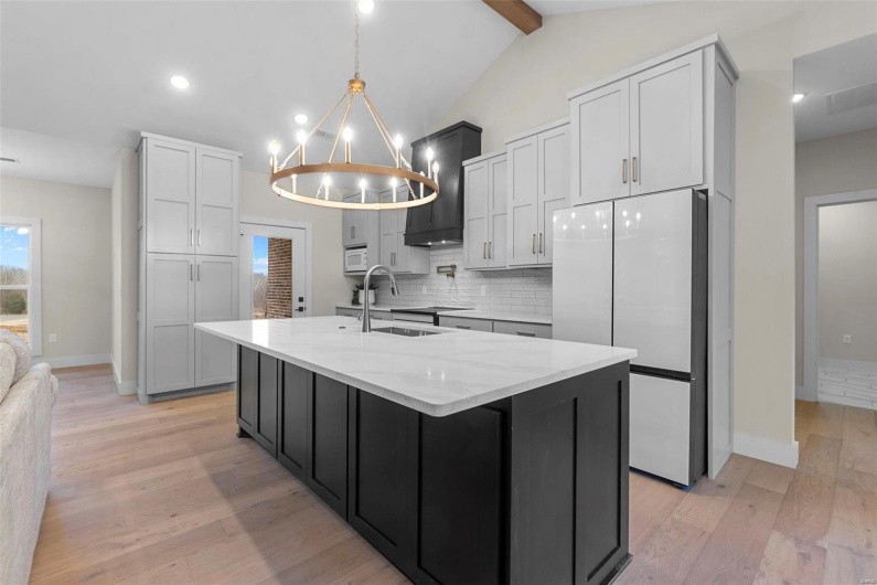 Kitchen featuring sink, light stone counters, refrigerator, an island with sink, and decorative backsplash