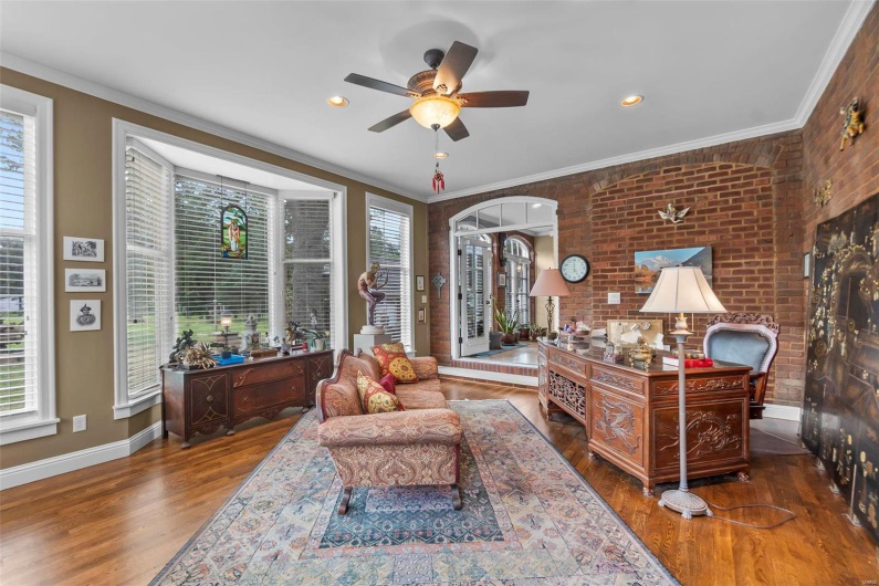 Living room featuring ornamental molding, brick wall, dark wood-type flooring, and ceiling fan