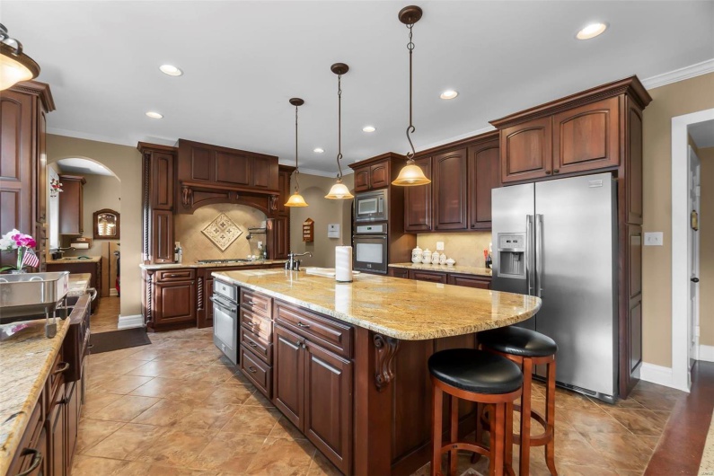 Kitchen featuring crown molding, a kitchen island with sink, backsplash, stainless steel appliances, and decorative light fixtures