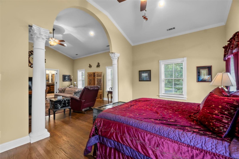 Bedroom featuring decorative columns, wood-type flooring, lofted ceiling, and ornamental molding
