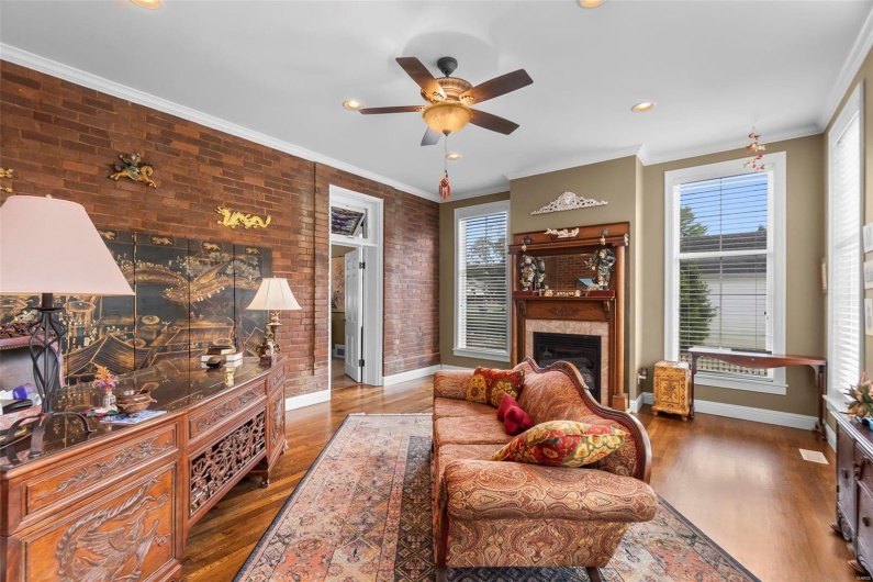 Living room featuring hardwood / wood-style flooring, ornamental molding, brick wall, and ceiling fan