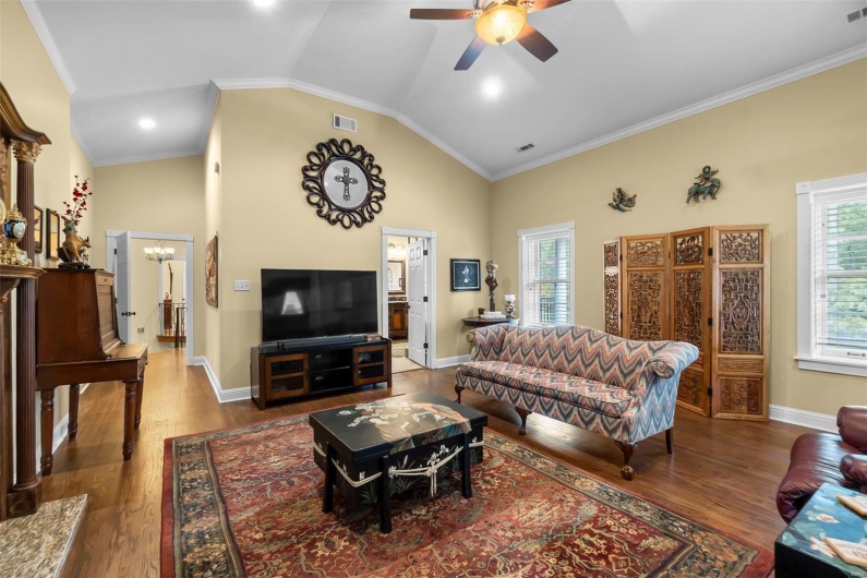 Living room with crown molding, wood-type flooring, ceiling fan with notable chandelier, and high vaulted ceiling