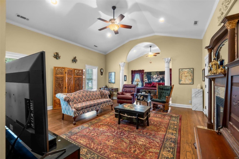 Living room with lofted ceiling, dark hardwood / wood-style flooring, ceiling fan, decorative columns, and a tiled fireplace