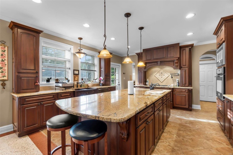 Kitchen with crown molding, hanging light fixtures, an island with sink, stainless steel appliances, and light stone countertops