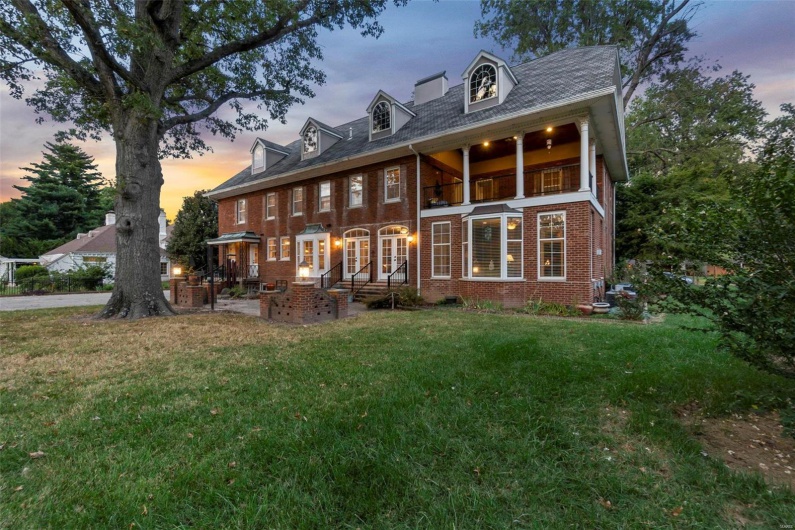 Back house at dusk featuring a lawn and a balcony