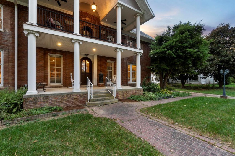 Exterior entry at dusk with a lawn, a balcony, ceiling fan, and covered porch