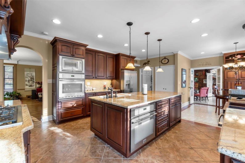 Kitchen featuring decorative light fixtures, a center island with sink, light stone countertops, and appliances with stainless steel finishes
