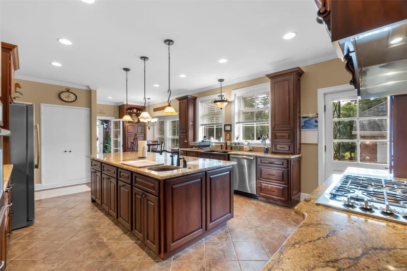 Kitchen with crown molding, light stone counters, pendant lighting, stainless steel appliances, and a kitchen island with sink