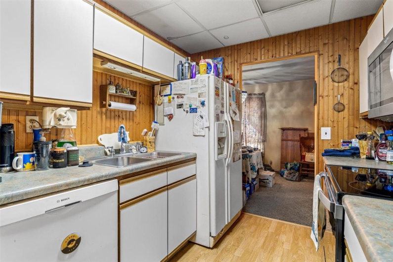 Kitchen featuring appliances with stainless steel finishes, sink, white cabinets, and wood walls