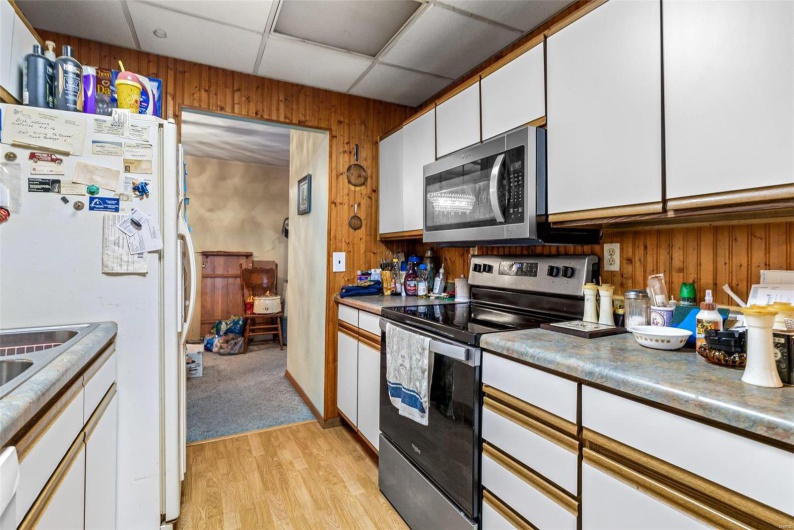 Kitchen featuring wood walls, white cabinets, light hardwood / wood-style floors, stainless steel appliances, and a drop ceiling