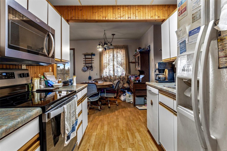 Kitchen with white cabinetry, a chandelier, hanging light fixtures, stainless steel appliances, and light hardwood / wood-style flooring