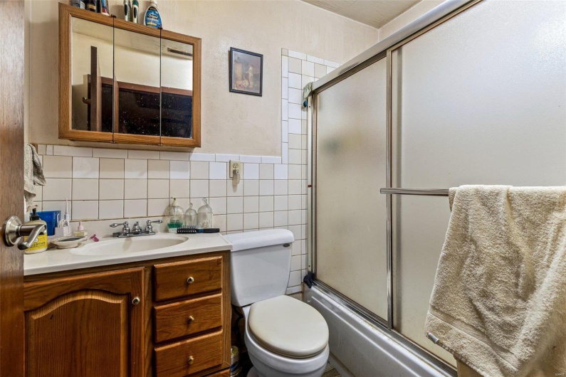 Full bathroom featuring tile walls, vanity, enclosed tub / shower combo, and toilet