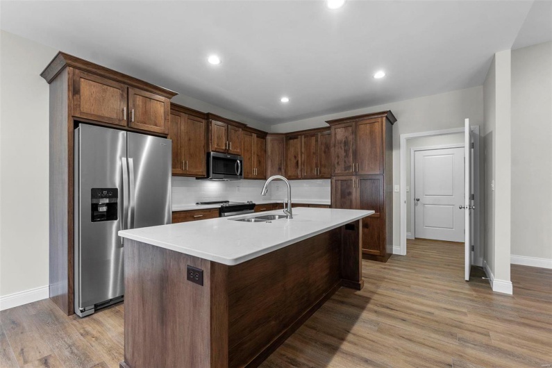 Kitchen with sink, backsplash, light wood-type flooring, stainless steel appliances, and a kitchen island with sink