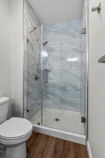 Bathroom with toilet, a shower with shower door, and wood-type flooring
