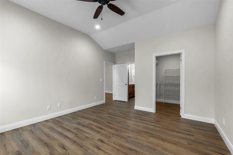 Unfurnished bedroom featuring a closet, a spacious closet, lofted ceiling, ceiling fan, and dark hardwood / wood-style floors