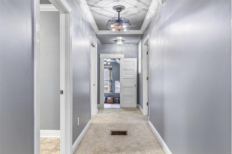 Hall featuring light carpet, crown molding, and an inviting chandelier