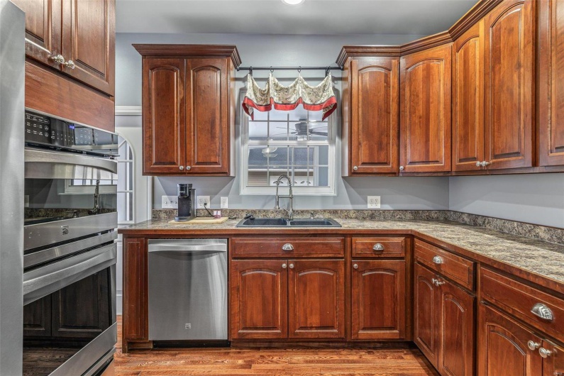 Kitchen with stainless steel appliances, light stone countertops, sink, and wood-type flooring