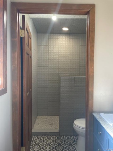 Bathroom with vanity, a tile shower, tile patterned floors, and toilet