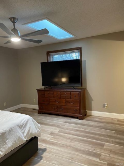Bedroom with ceiling fan, a skylight, light hardwood / wood-style floors, and a textured ceiling