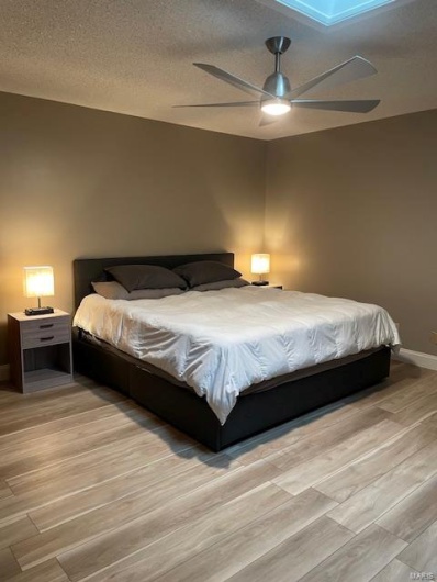Bedroom with ceiling fan, light hardwood / wood-style flooring, and a textured ceiling