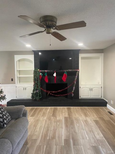 Living room featuring built in shelves, a fireplace, a textured ceiling, and light hardwood / wood-style flooring