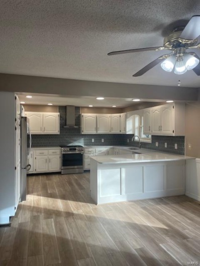 Kitchen with white cabinetry, stainless steel appliances, kitchen peninsula, and wall chimney exhaust hood