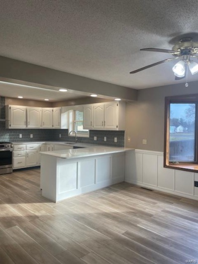 Kitchen featuring white cabinetry, sink, light hardwood / wood-style flooring, kitchen peninsula, and stainless steel electric range