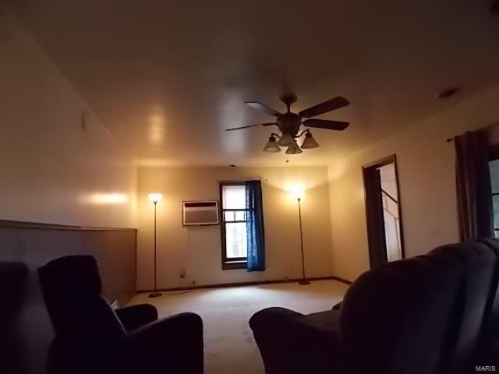 Carpeted living room featuring a wall mounted air conditioner and ceiling fan