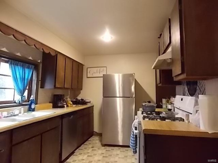 Kitchen with dark brown cabinetry, white range oven, sink, and stainless steel refrigerator