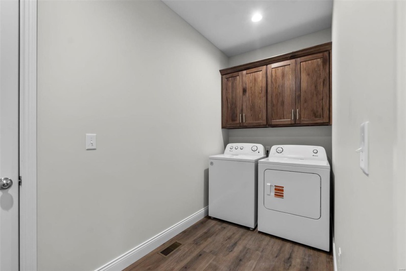 Clothes washing area with cabinets, washing machine and dryer, and dark hardwood / wood-style floors