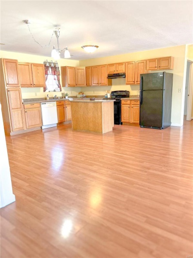 Kitchen featuring light wood-style floors, a center island, hanging light fixtures, under cabinet range hood, and black appliances