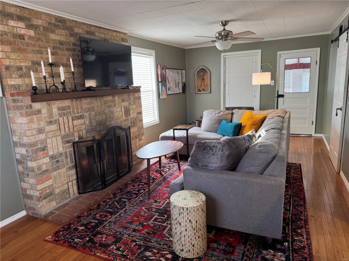 Living room featuring crown molding, wood-type flooring, a barn door, and ceiling fan