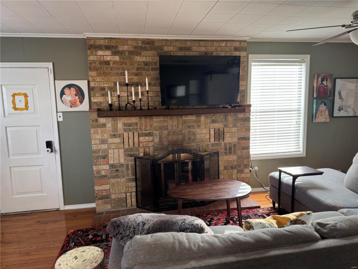 Living room featuring crown molding, hardwood / wood-style floors, ceiling fan, and a fireplace