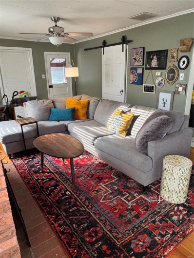 Living room with crown molding, ceiling fan, a barn door, and hardwood / wood-style flooring