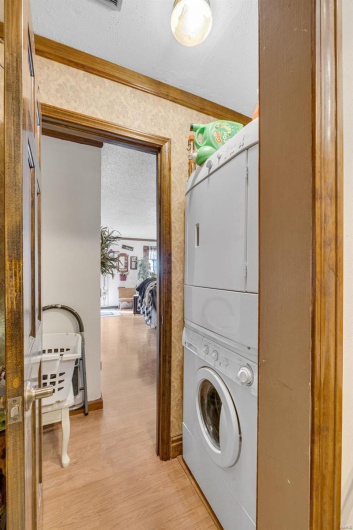 Clothes washing area featuring ornamental molding, light hardwood / wood-style floors, a textured ceiling, and stacked washing maching and dryer