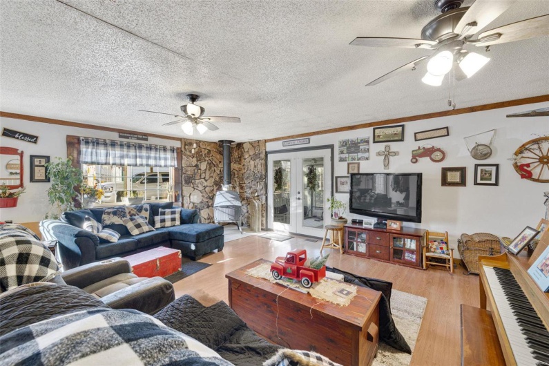 Living room featuring a wood stove, ceiling fan, light hardwood / wood-style floors, a textured ceiling, and french doors