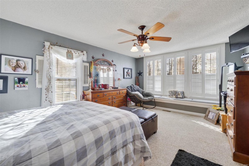 Carpeted bedroom featuring ceiling fan, multiple windows, and a textured ceiling