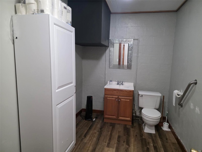 Half bath with concrete block wall, toilet, wood finished floors, and vanity