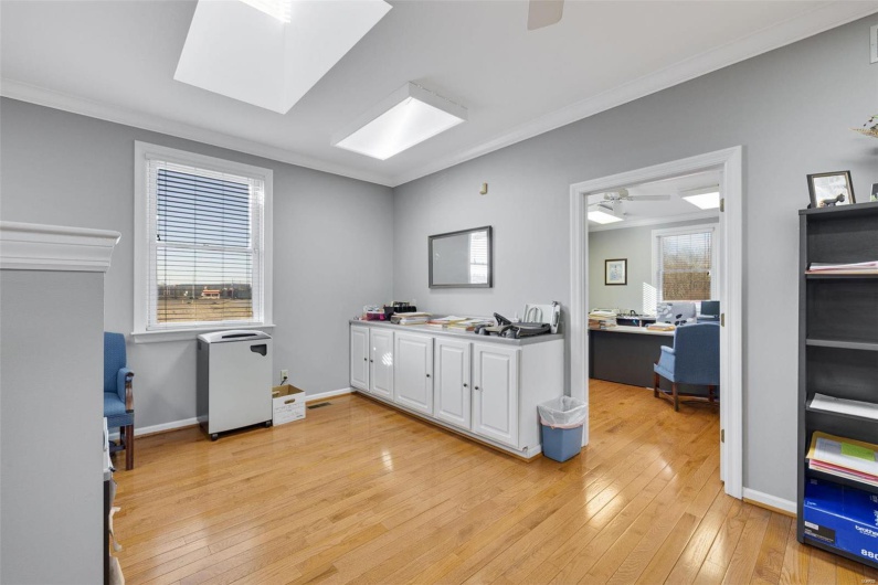 Kitchen featuring crown molding, ceiling fan, white cabinetry, a skylight, and light wood-type flooring