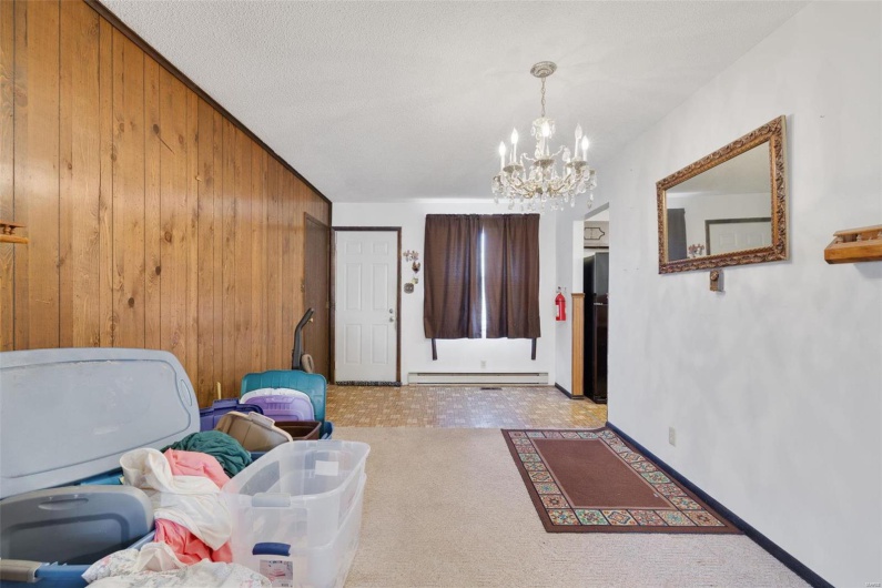 Carpeted foyer featuring a baseboard radiator, a chandelier, and wooden walls