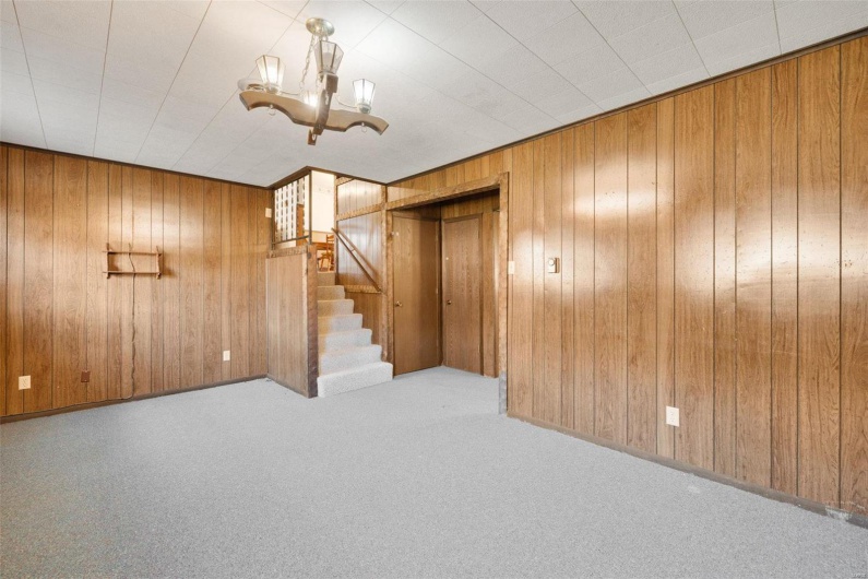 Basement featuring an inviting chandelier, light colored carpet, and wood walls