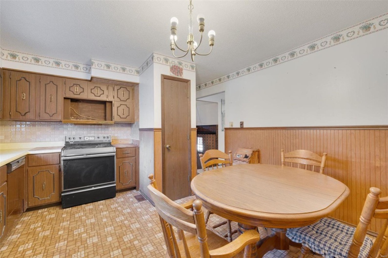 Kitchen with a textured ceiling, wood walls, an inviting chandelier, and stainless steel electric range