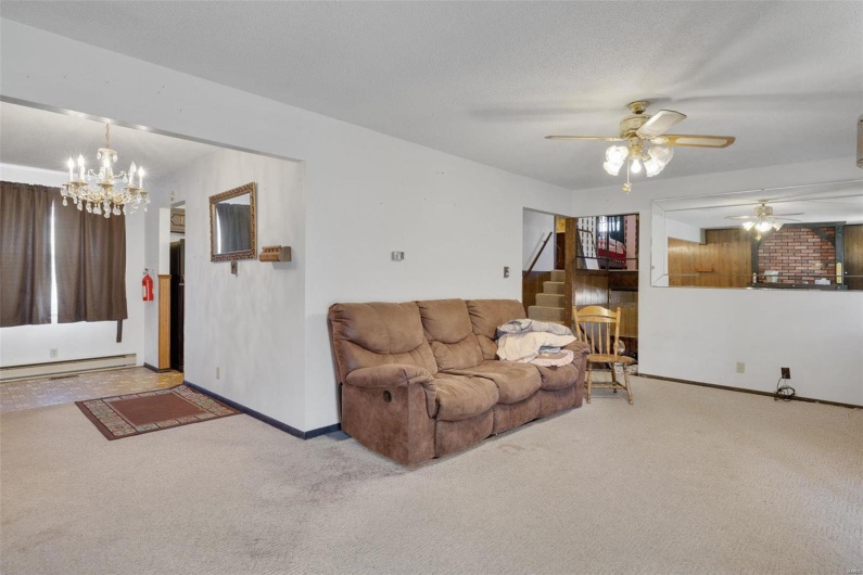 Carpeted living room with ceiling fan with notable chandelier, a baseboard radiator, and a textured ceiling