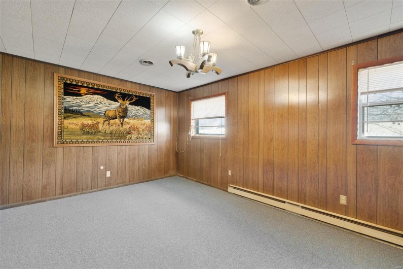 Unfurnished room featuring baseboard heating, wooden walls, carpet flooring, and an inviting chandelier