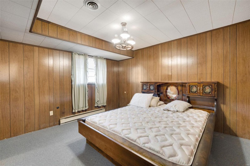 Carpeted bedroom featuring a baseboard radiator, a chandelier, and wood walls
