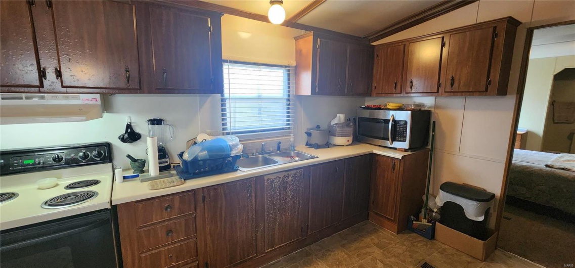 Kitchen featuring vaulted ceiling, dark brown cabinetry, sink, and electric range