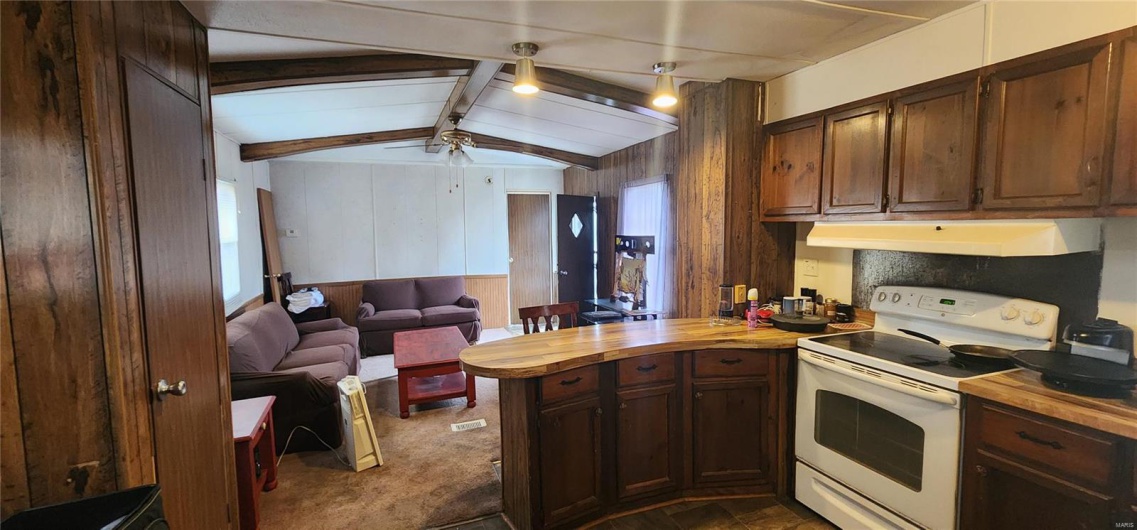 Kitchen with vaulted ceiling with beams, wooden counters, wooden walls, and electric stove