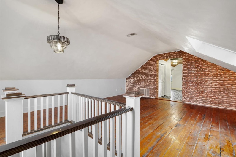 Third floor studio. Additional living space featuring brick wall, wood-type flooring, and vaulted ceiling with skylight