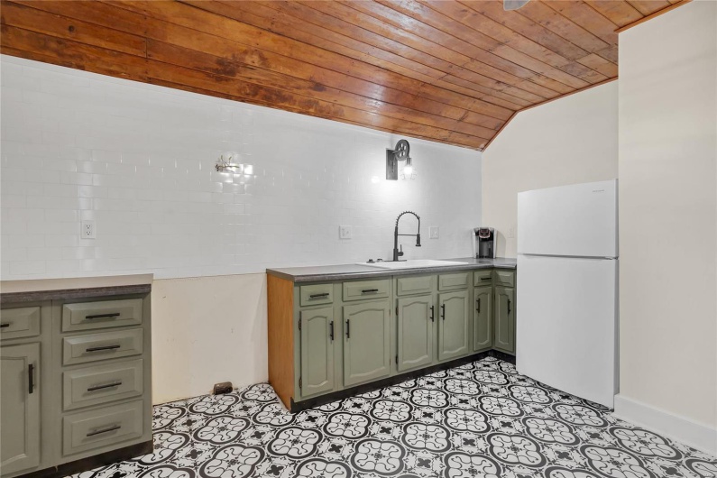 Third floor studio. Kitchen with vaulted ceiling, sink, white fridge, green cabinetry, and wooden ceiling